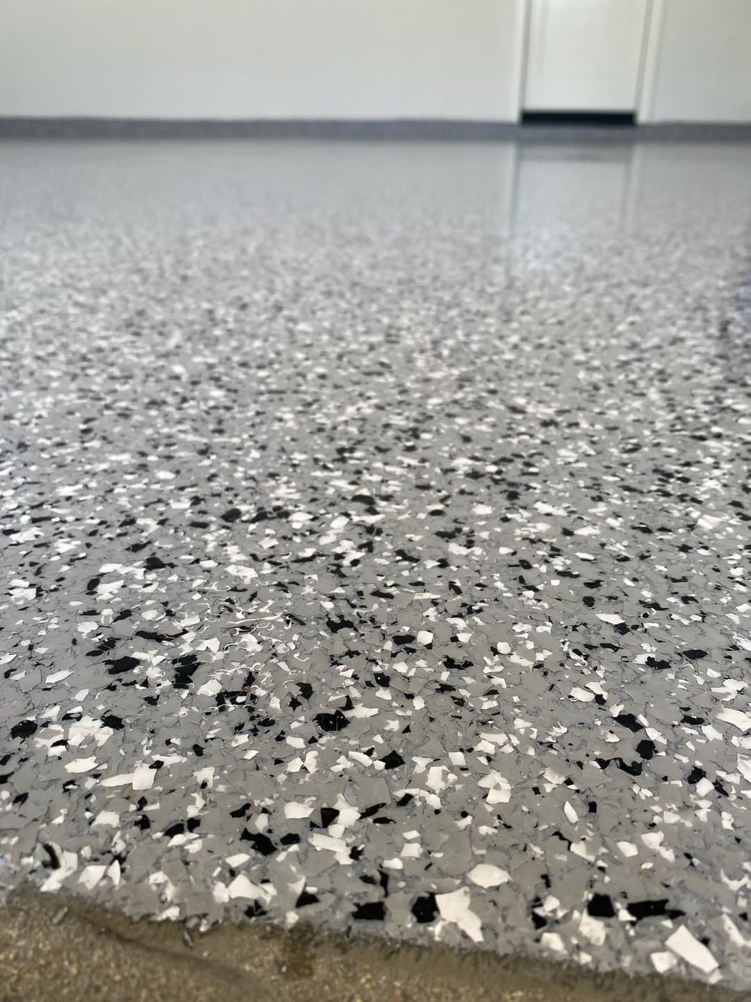 Close-up of a textured gray epoxy floor with black and white flakes in a clean garage.
