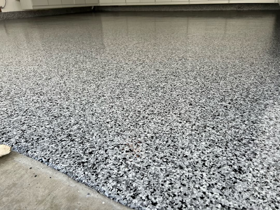 Close-up of a polished gray epoxy floor with a glossy finish and decorative chips.