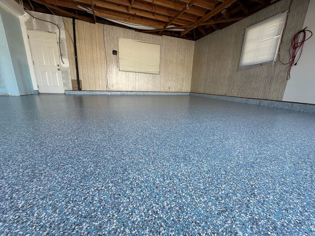 Blue speckled epoxy floor in a spacious room with bare walls and wooden ceiling beams.