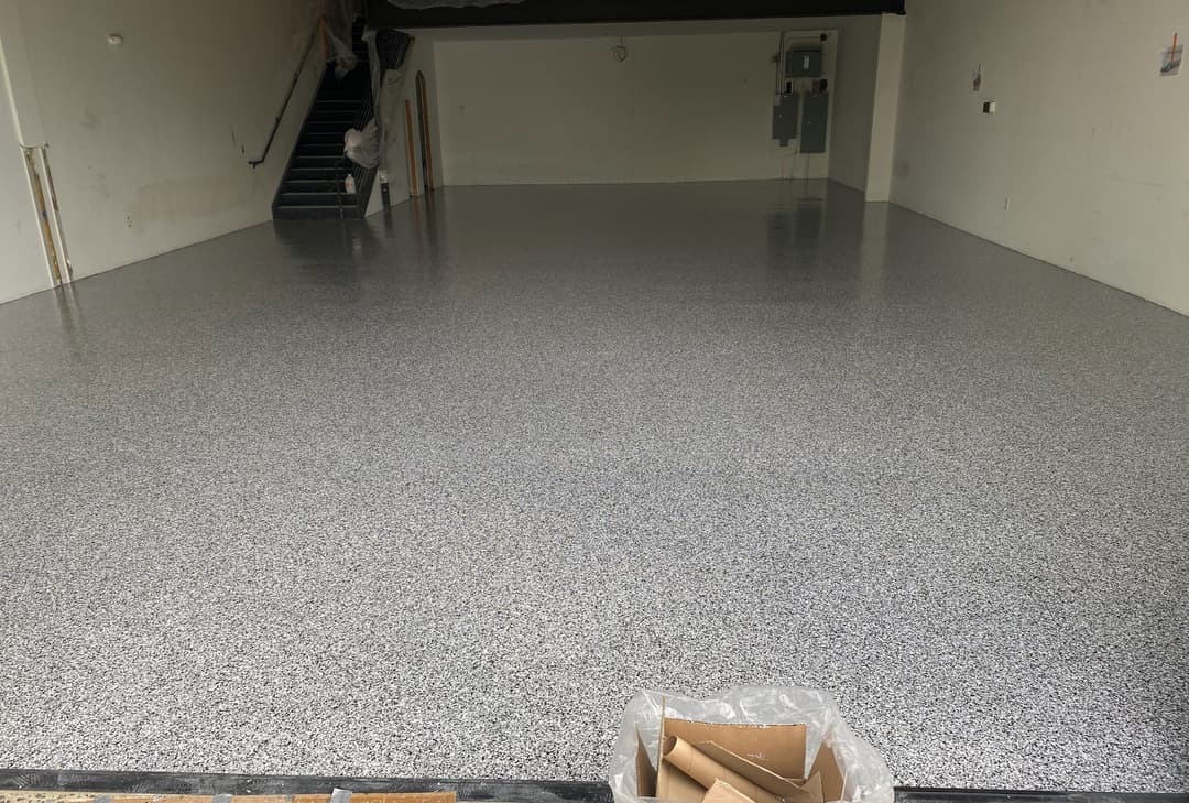 Newly finished epoxy garage floor with a gray and white speckled design, clean and empty space.