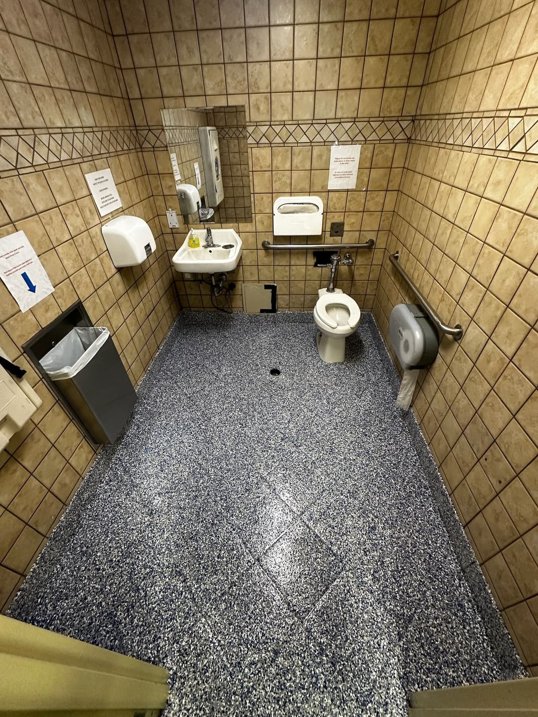 Clean restroom interior with tiled walls, toilet, sink, and hand dryer on textured floor.