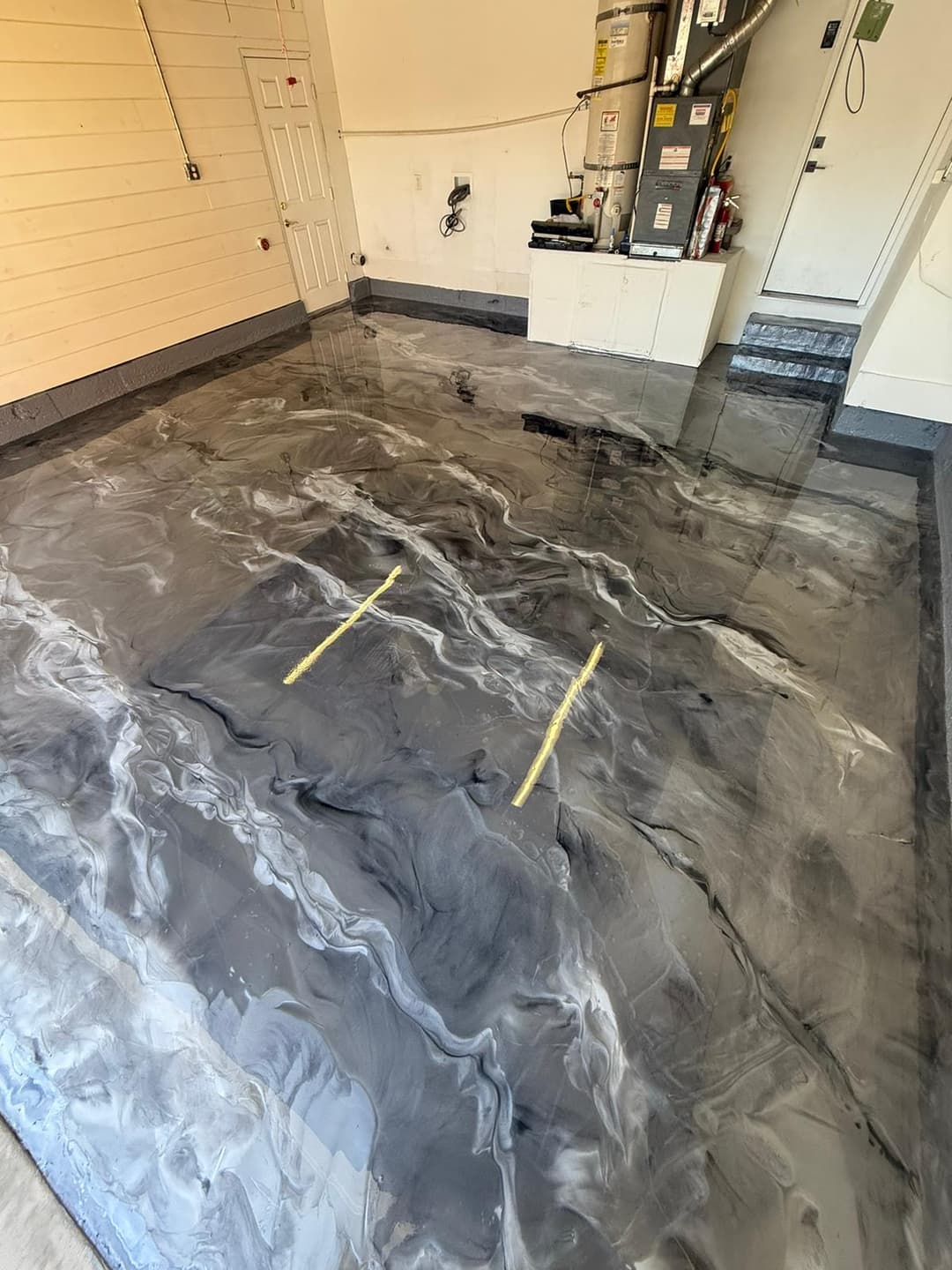 Epoxy-coated garage floor with black and gray swirls and yellow markings for sectioning.