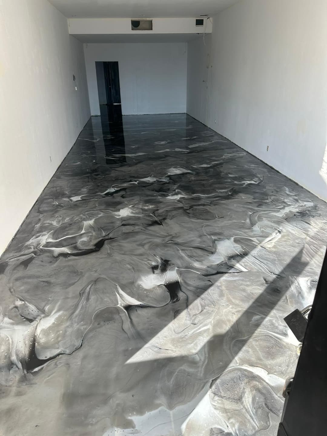 Modern empty room with a sleek black and white marbled epoxy floor finish.