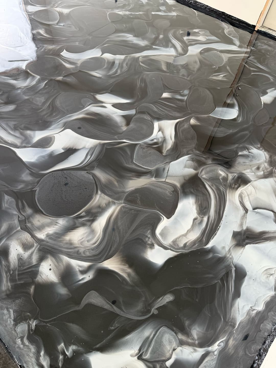 Abstract swirling black and gray surface with glossy finish, resembling liquid art.