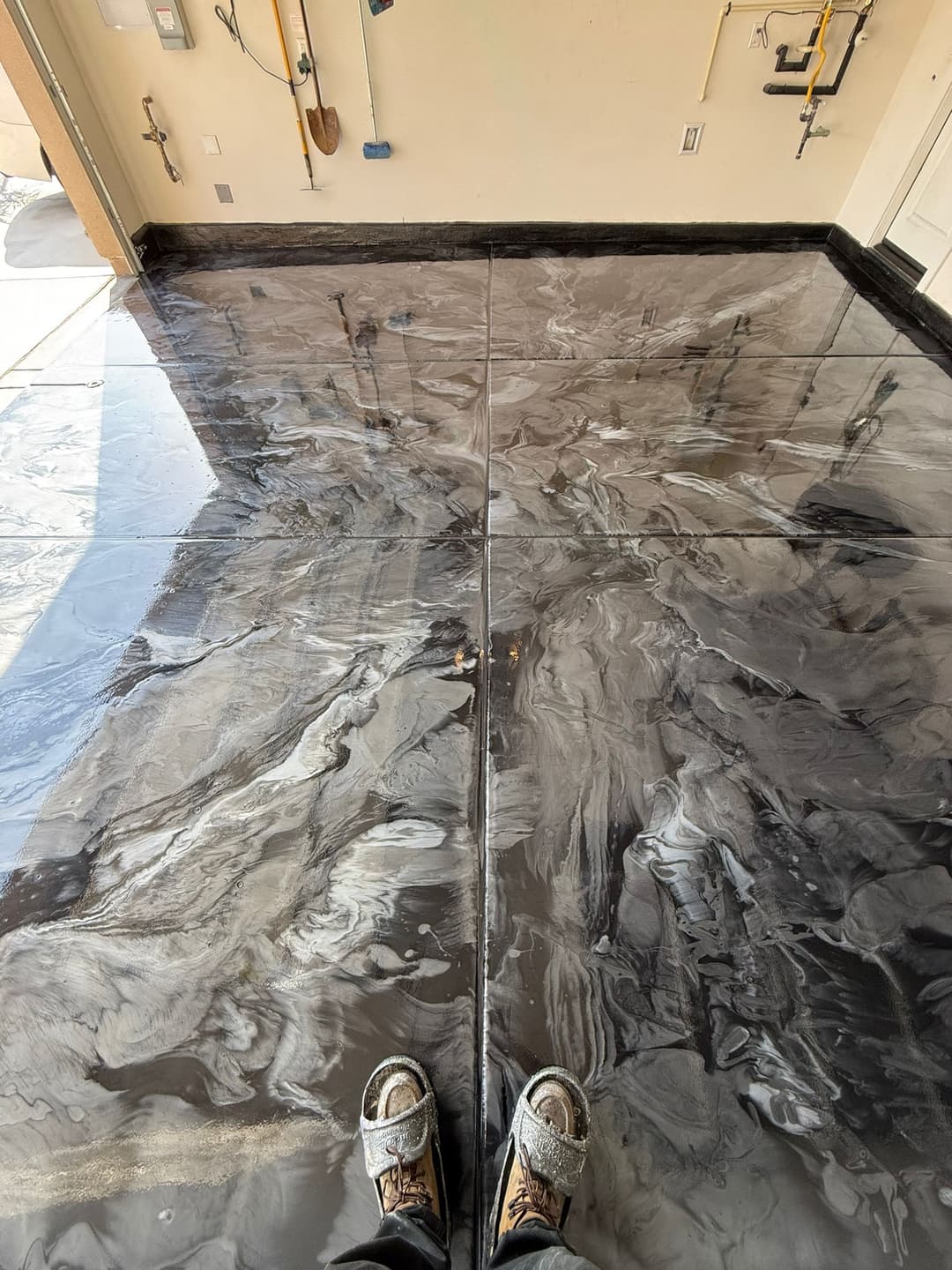 Glossy black and white epoxy floor in a garage, with tools visible on the wall.