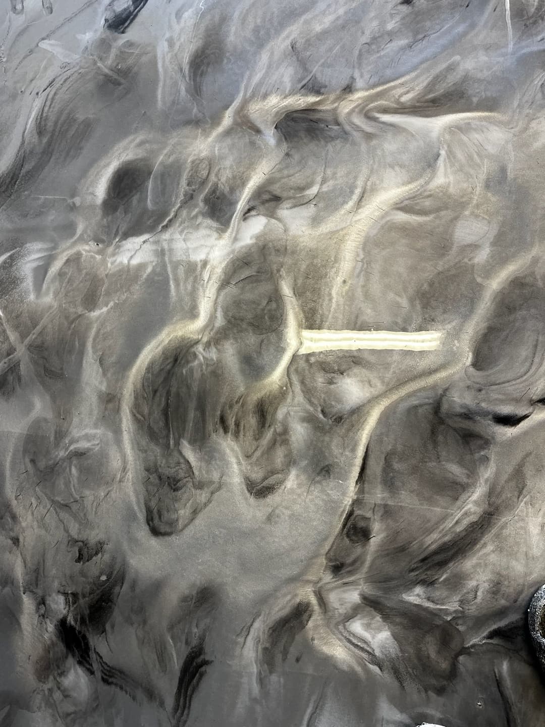 Aerial view of textured dark sand with light streaks creating abstract patterns.