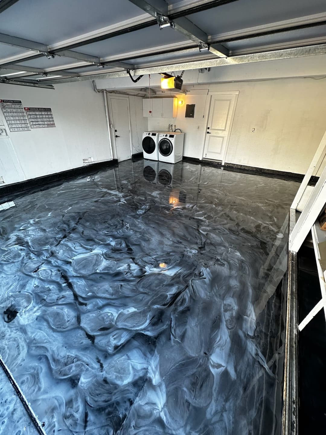 Glossy black and white epoxy floor in a garage with laundry area in the background.