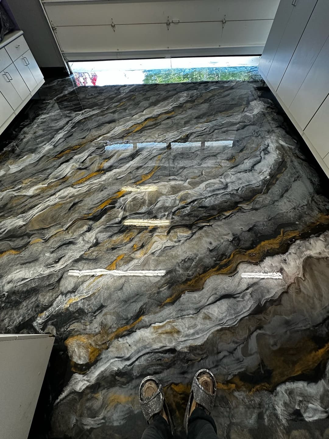 Stylish black and gold epoxy resin floor with person’s feet in modern interior space.