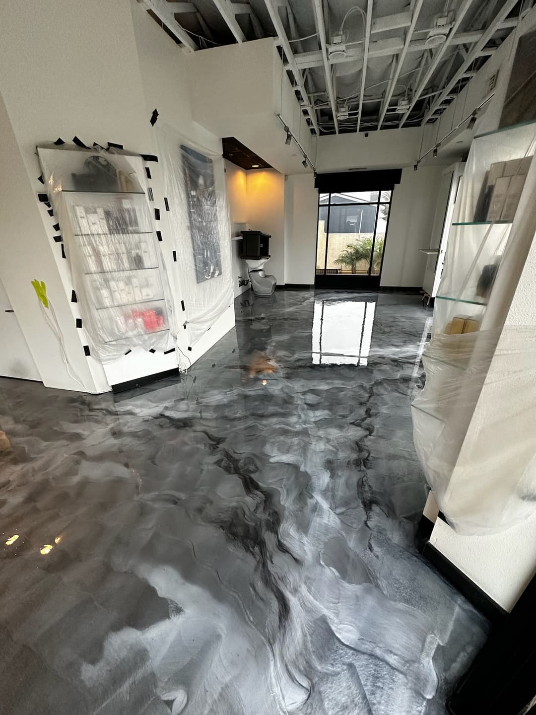 Modern interior with epoxy floor and partially covered furniture in a bright, open space.