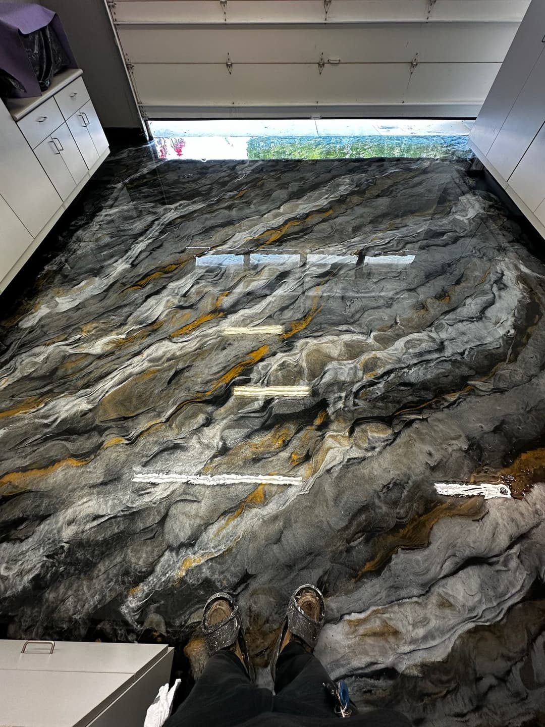 Artistic epoxy river floor with black, gray, and gold patterns in a modern garage setting.