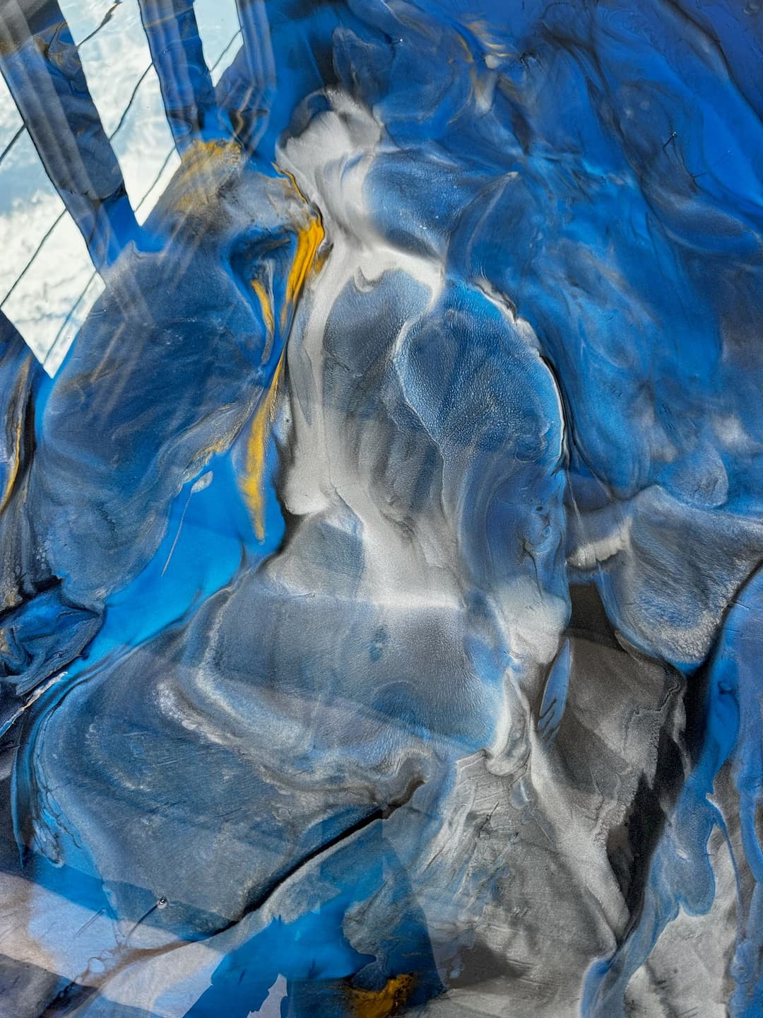 Abstract painting featuring swirling blue, black, and white textures with golden accents.
