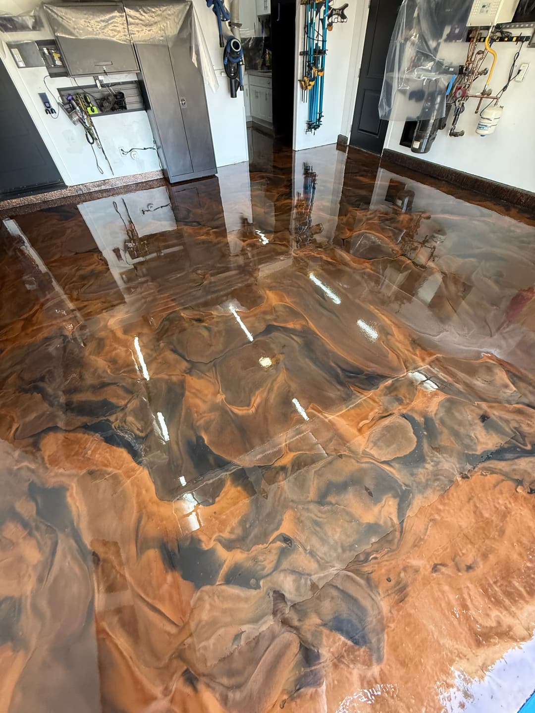 Epoxy resin garage floor with swirling brown and black patterns, reflecting overhead lights.