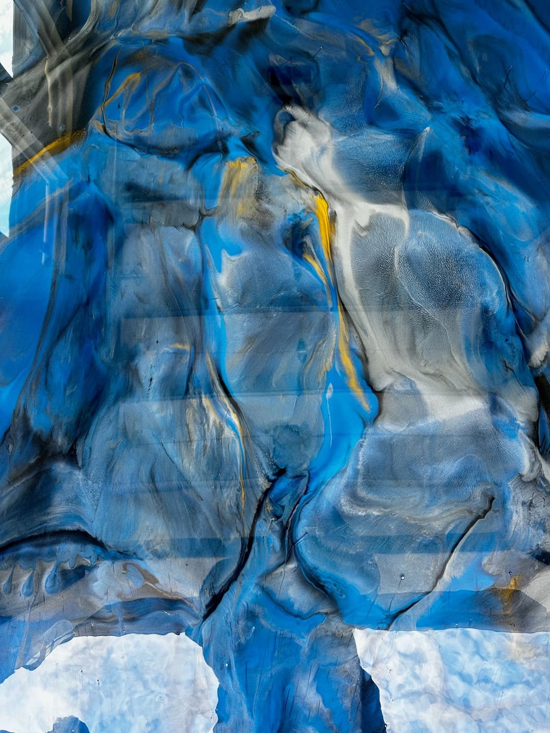 Abstract blue and gray fluid art with swirling patterns and touches of yellow highlights.