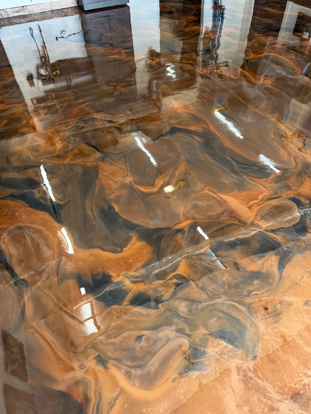 Beautiful epoxy resin floor showcasing rich swirls of orange and black colors in a glossy finish.
