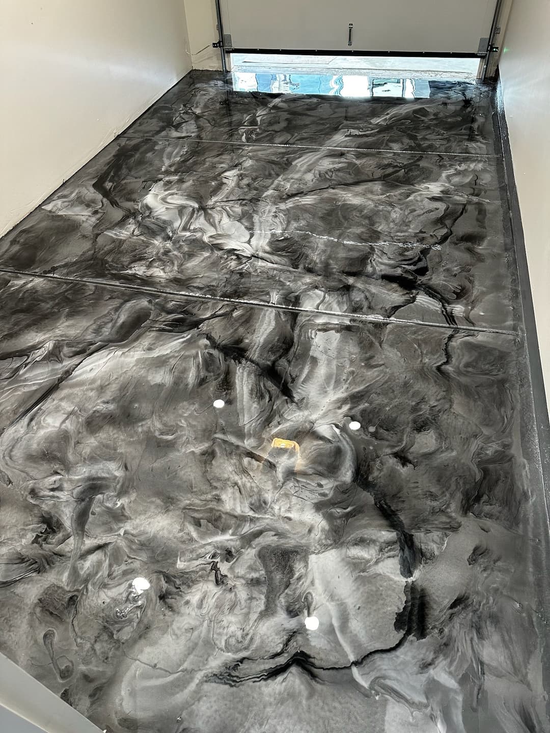 Polished black and gray epoxy garage floor with swirling patterns and light reflections.