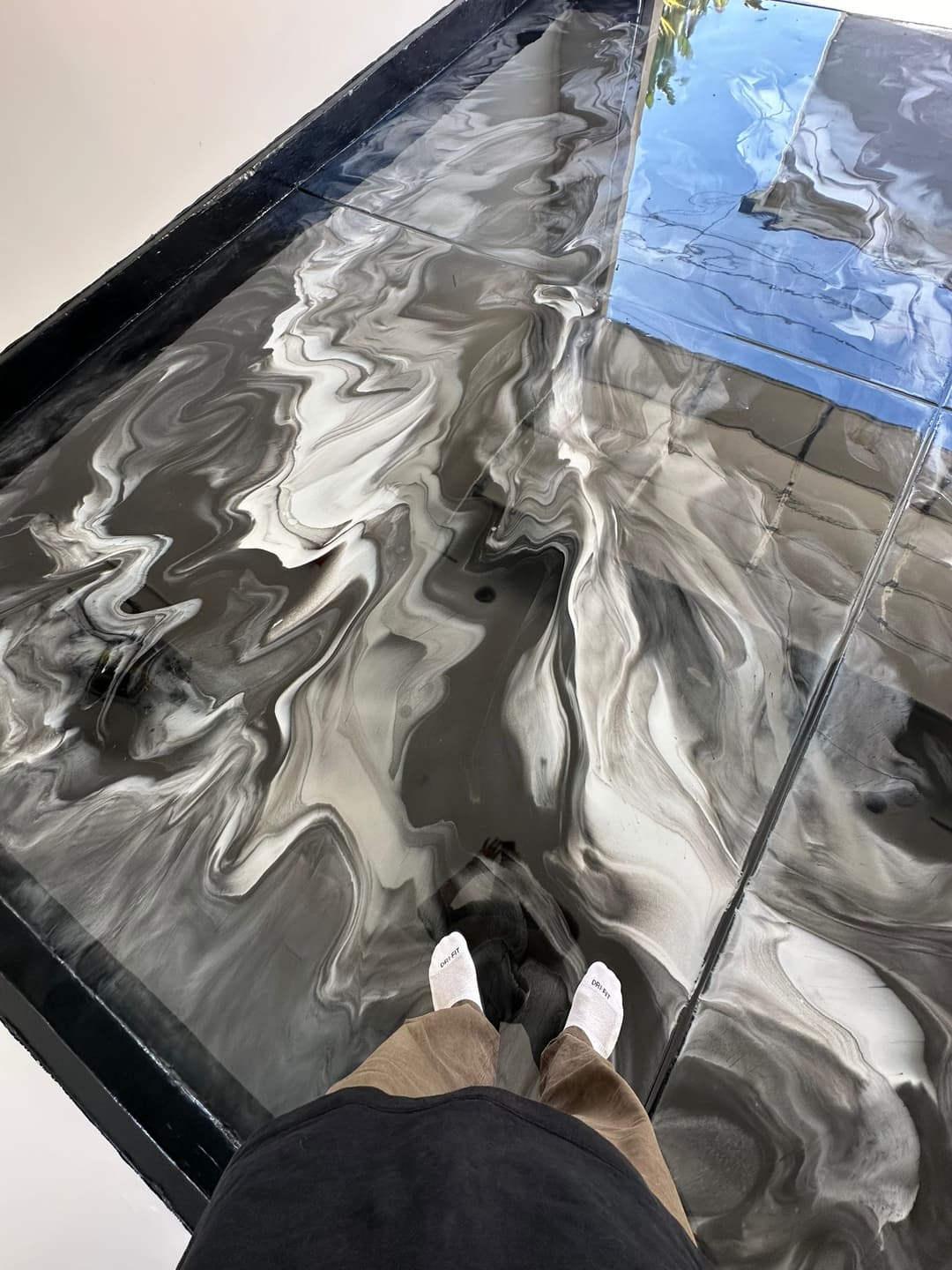 Person standing on a glossy, abstract black and white epoxy floor with reflections.