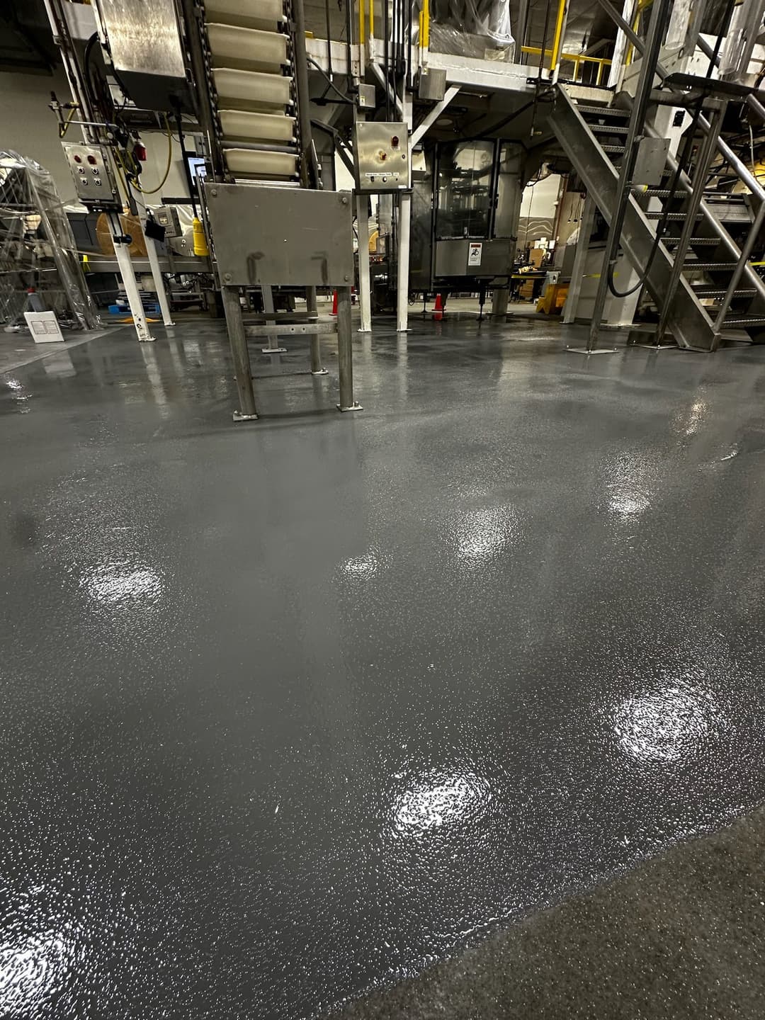 Industrial facility with freshly coated gray epoxy flooring and visible machinery in background.