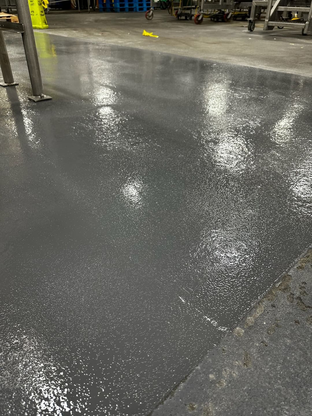 Shiny gray epoxy floor in industrial setting with bright overhead lights reflecting.