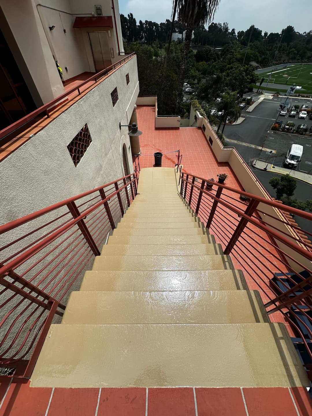 Staircase viewed from above, leading down to a parking area with green landscaping.