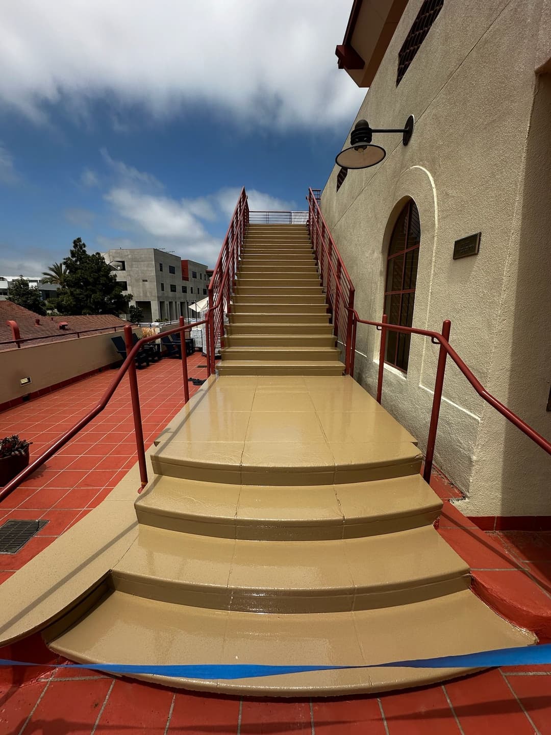 Staircase with railing and smooth surface, leading to a building entrance under cloudy sky.